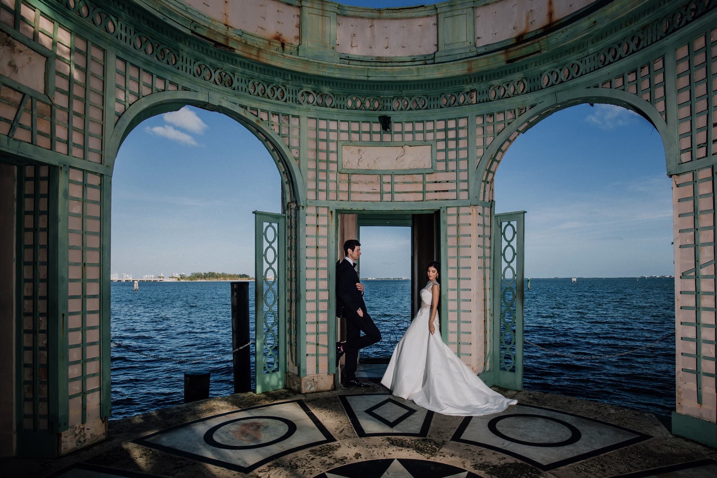 Bride and groom framed by the bayfront pavilion arches over Biscayne Bay — Vizcaya Museum and Gardens