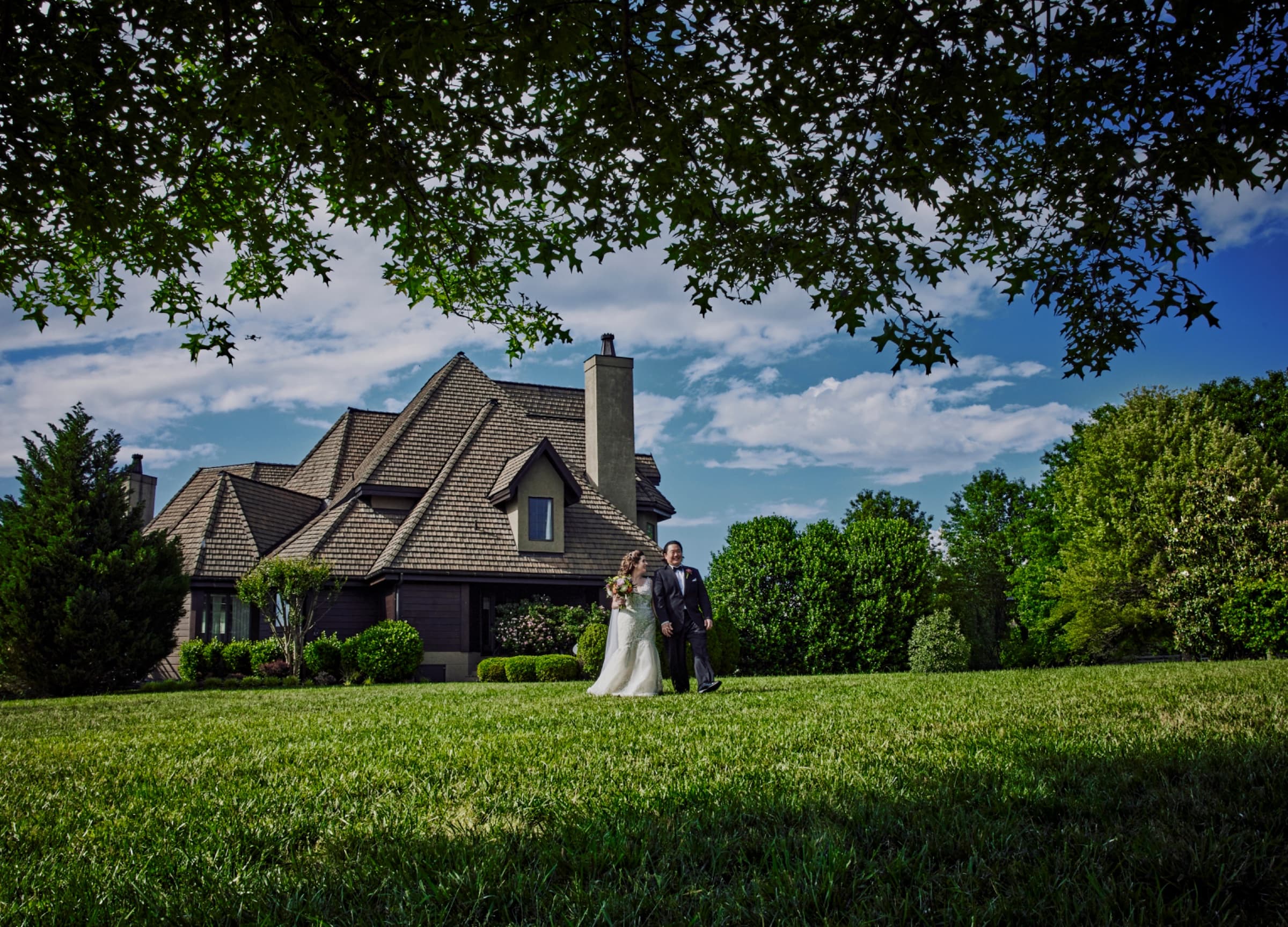 Couple crossing the lawn framed by oak branches with the manor behind — Champagne Manor wedding venue, Monroe, North Carolina