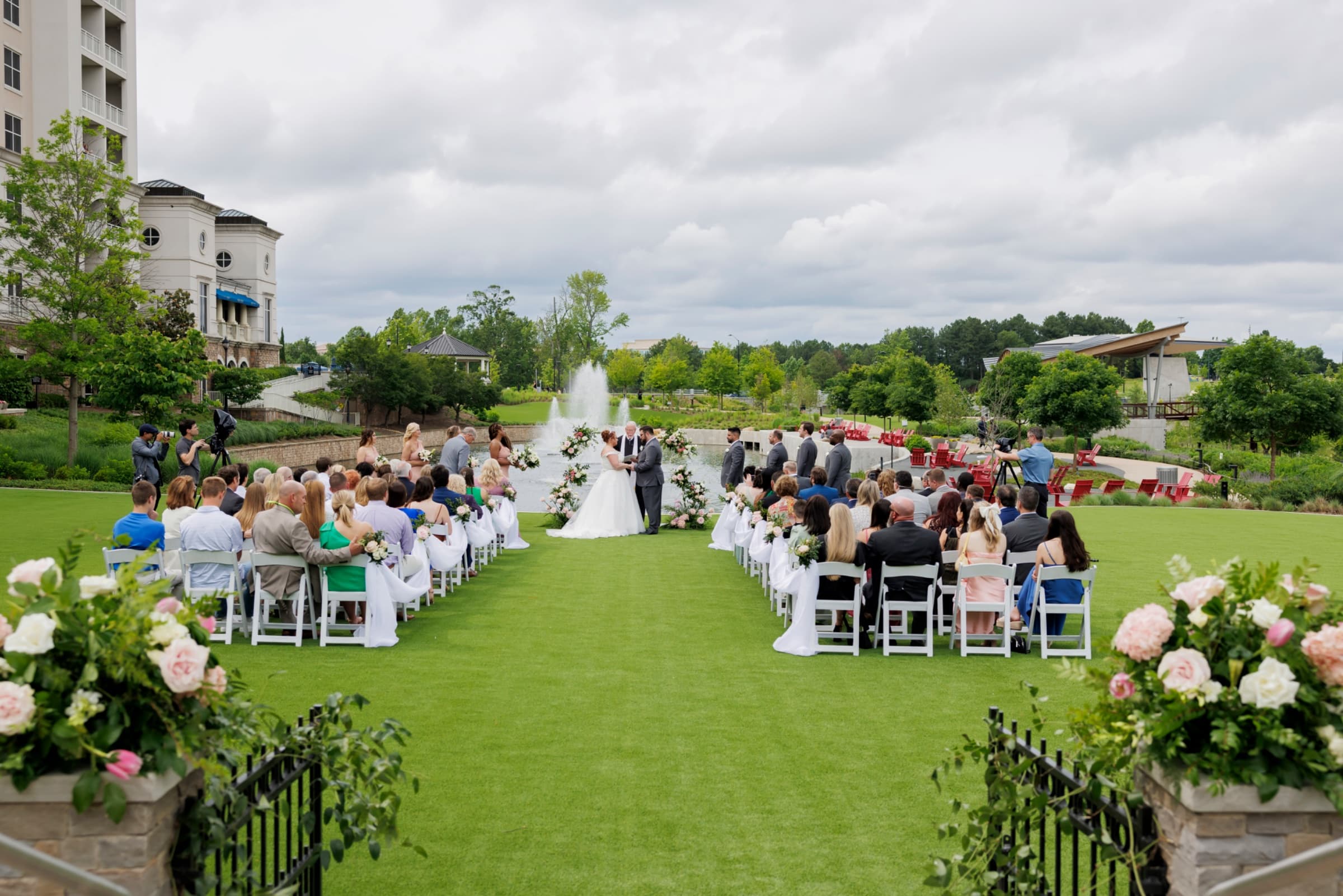 Lawn ceremony beside the fountain lake with blush floral arch — The Ballantyne Hotel wedding venue, Charlotte, North Carolina