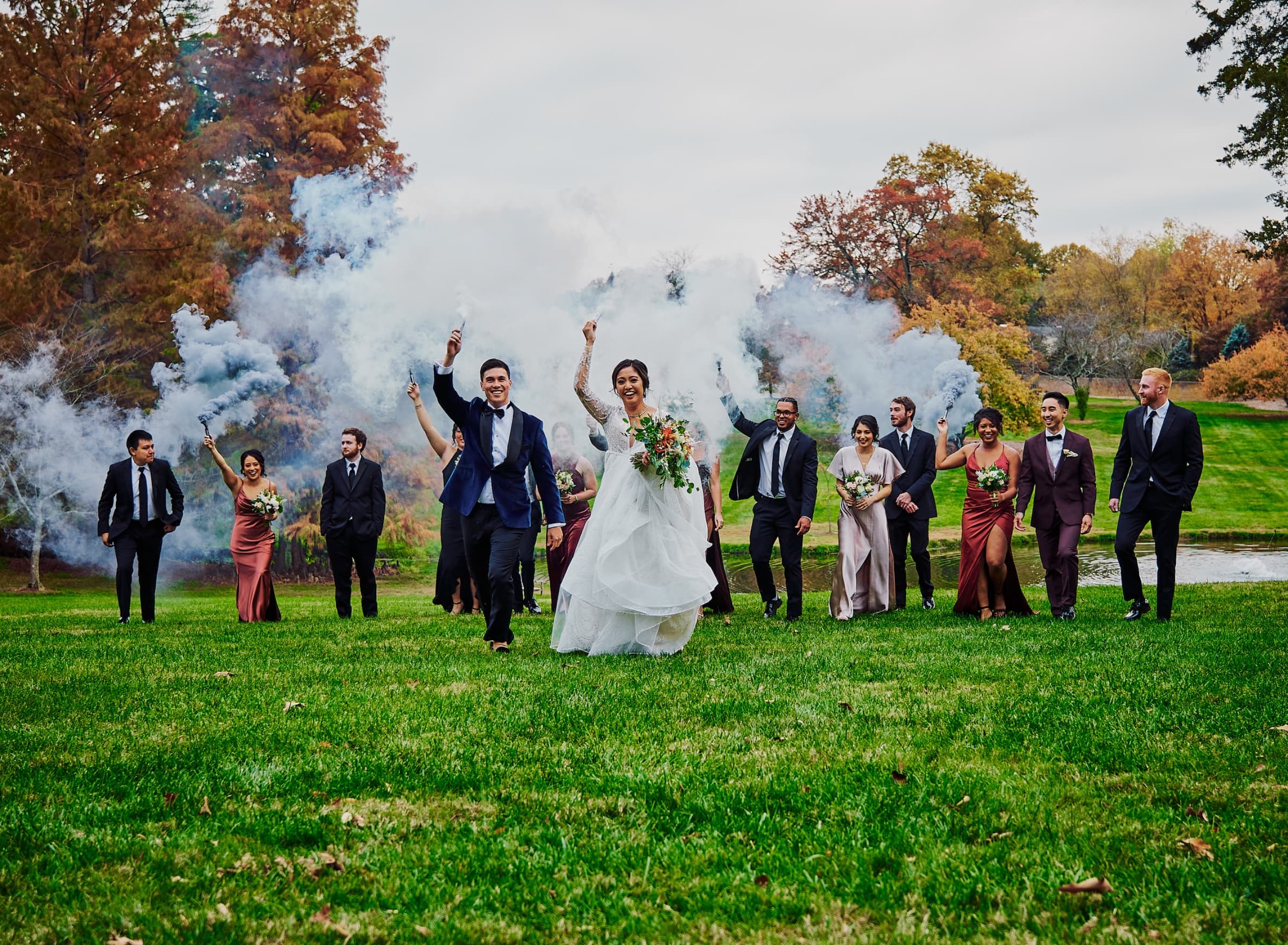Wedding party walking out through coloured smoke bombs in autumn colour — The Graylyn Estate