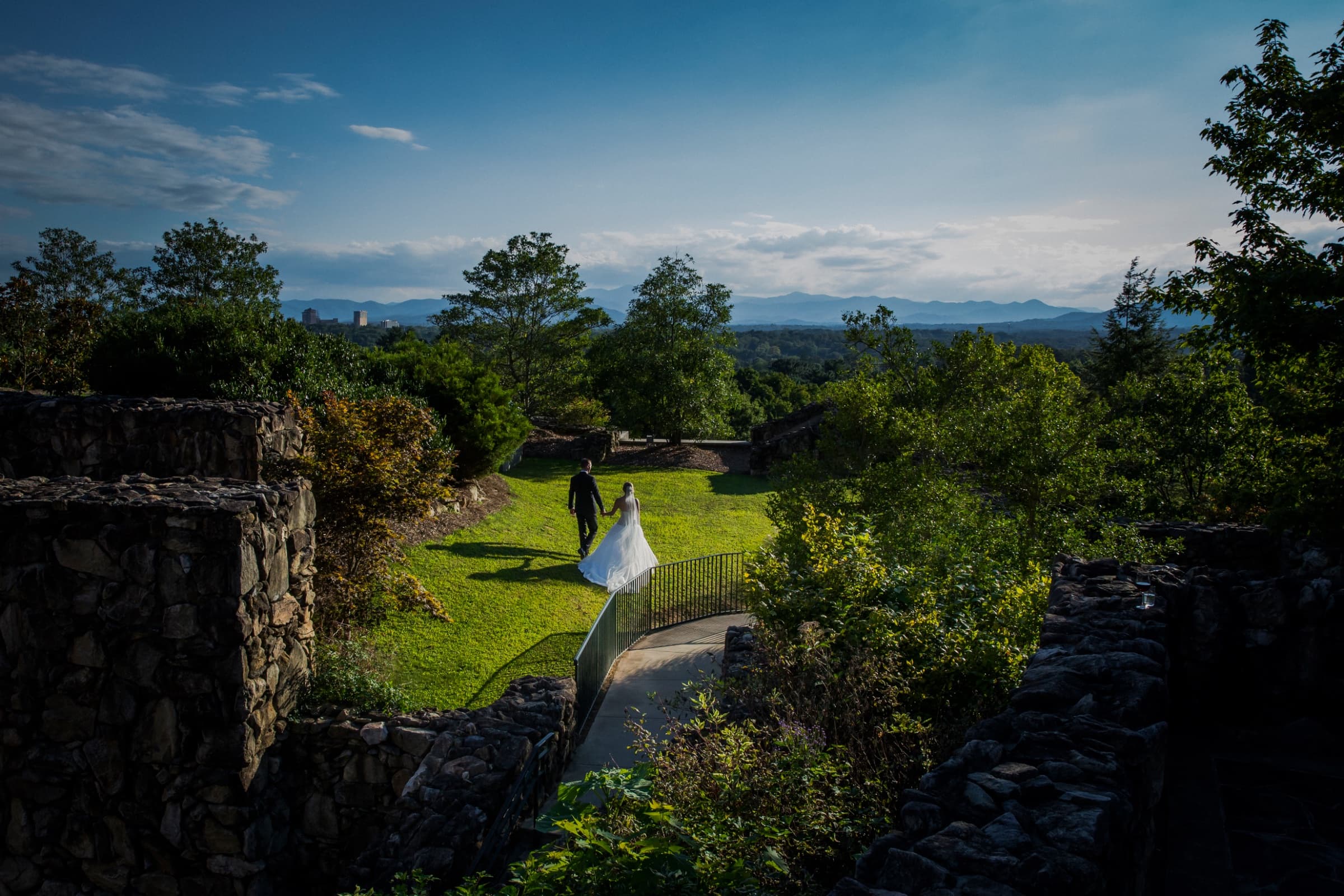 Couple on the lawn between the stone terraces with mountains beyond — The Omni Grove Park Inn