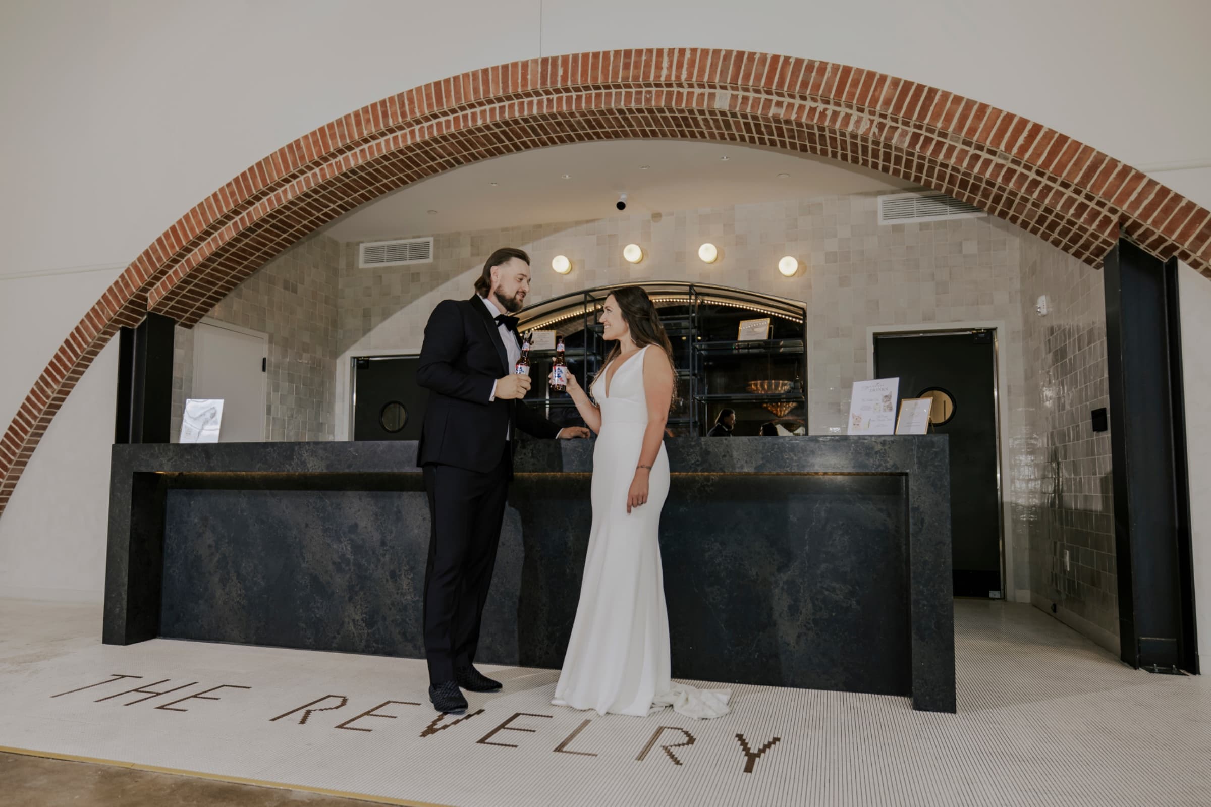 Couple toasting at the bar beneath the brick archway — The Revelry North End wedding venue, Charlotte, North Carolina