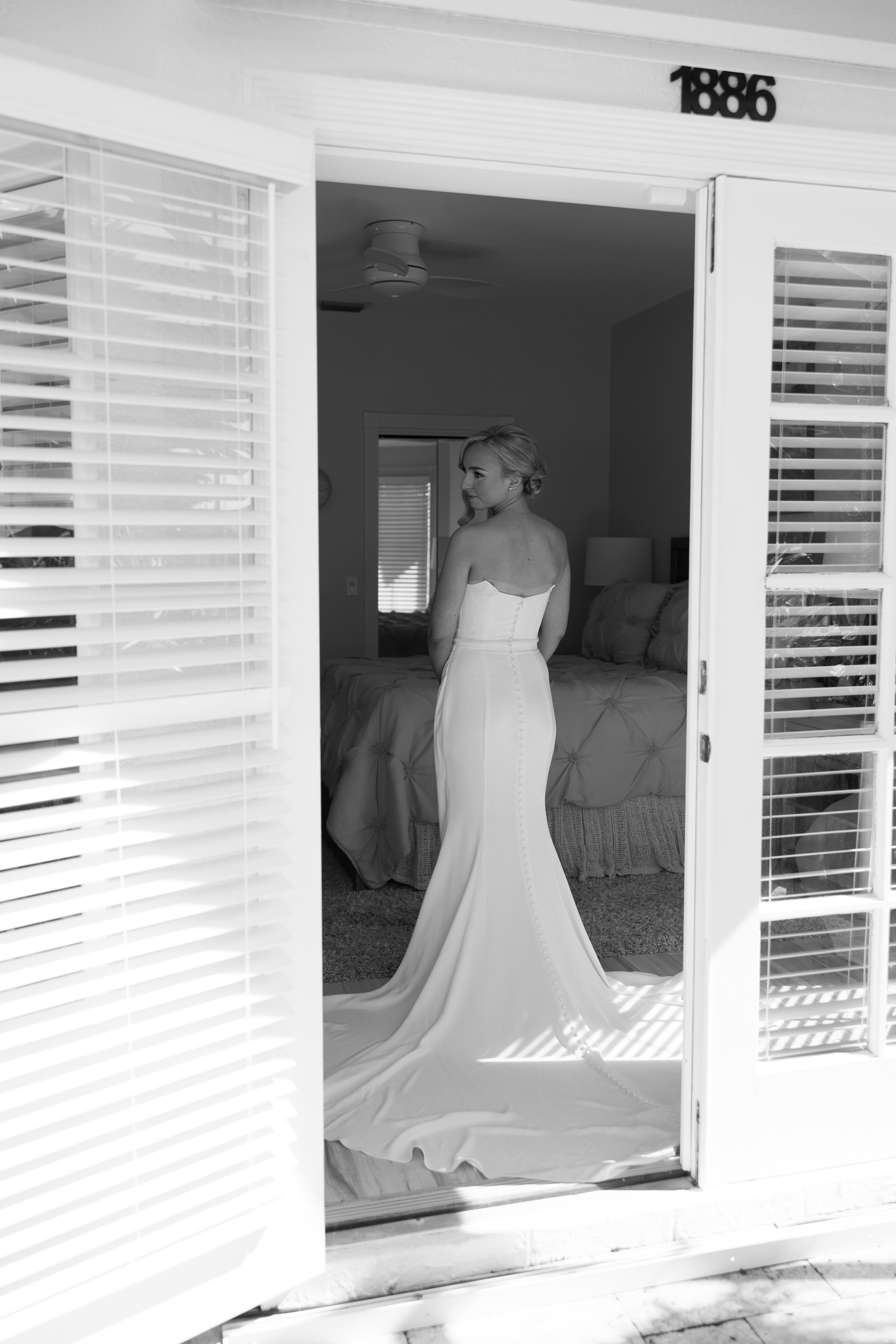 Bride looking back over her shoulder, framed by open shutters before the ceremony — black and white Florida wedding portrait