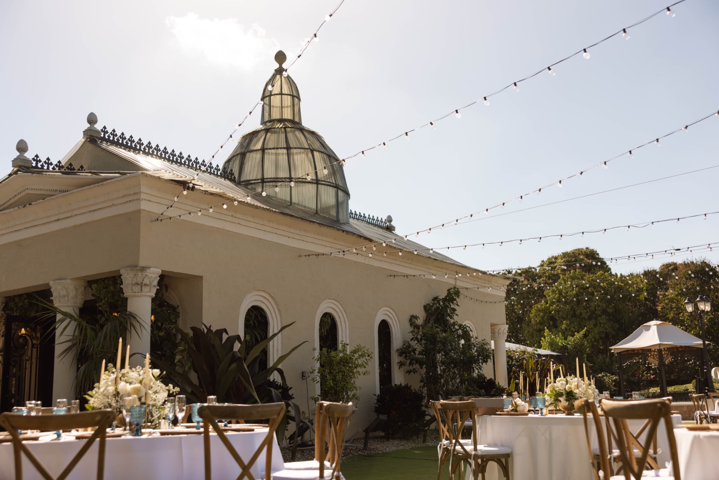 String lights across the courtyard beneath the glass dome, tables set with taper candles and white florals — Villa Toscana M…